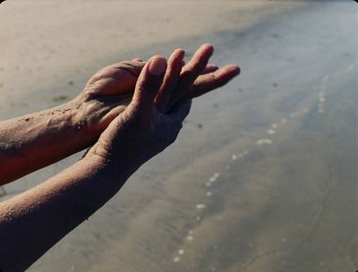 Film still from Tenzin Phuntsog’s „Pala Amala“. Two sandy hands in front of a coastal strip.