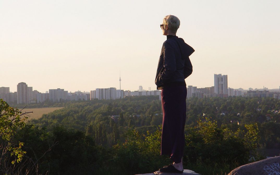 Film still from THE INVISIBLE FRAME: Tilda Swinton looks from a slightly elevated position at a row of skyscrapers, with the Berlin TV tower in the background.