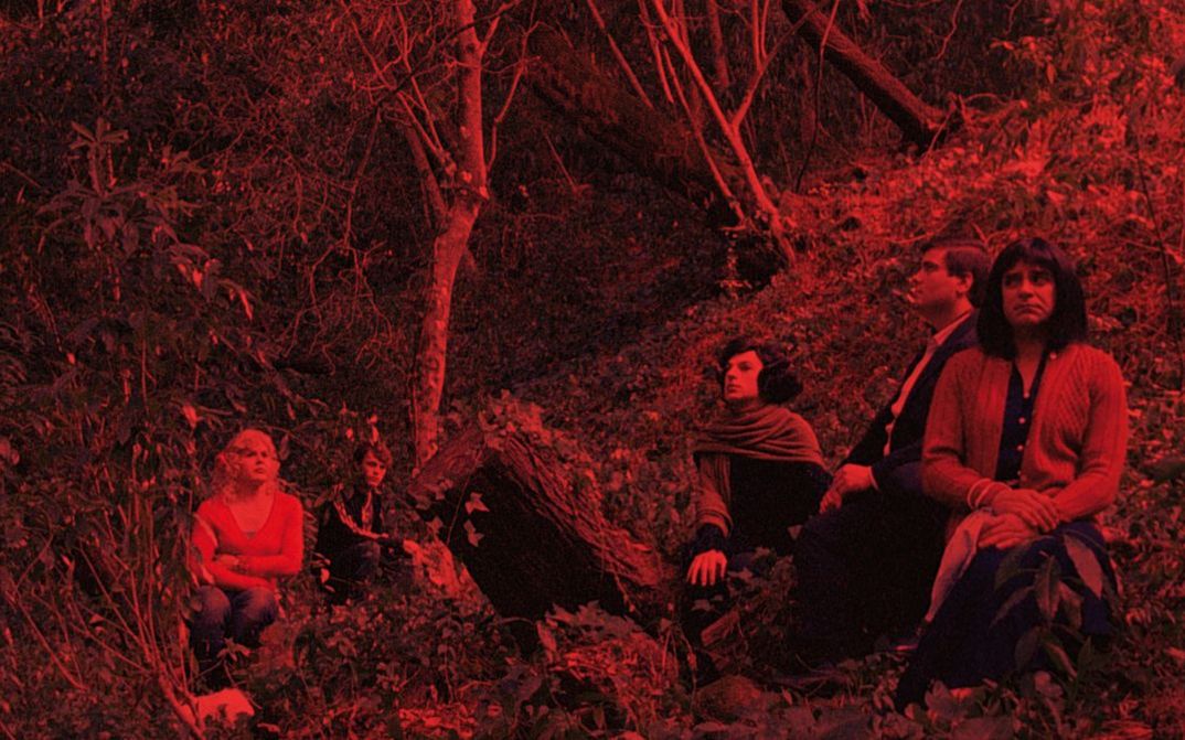 Filmstill aus MORRER COMO UM HOMEM: Ein rot eingefärbtes Bild einer Gruppe von Menschen, die in einem Wald sitzt.