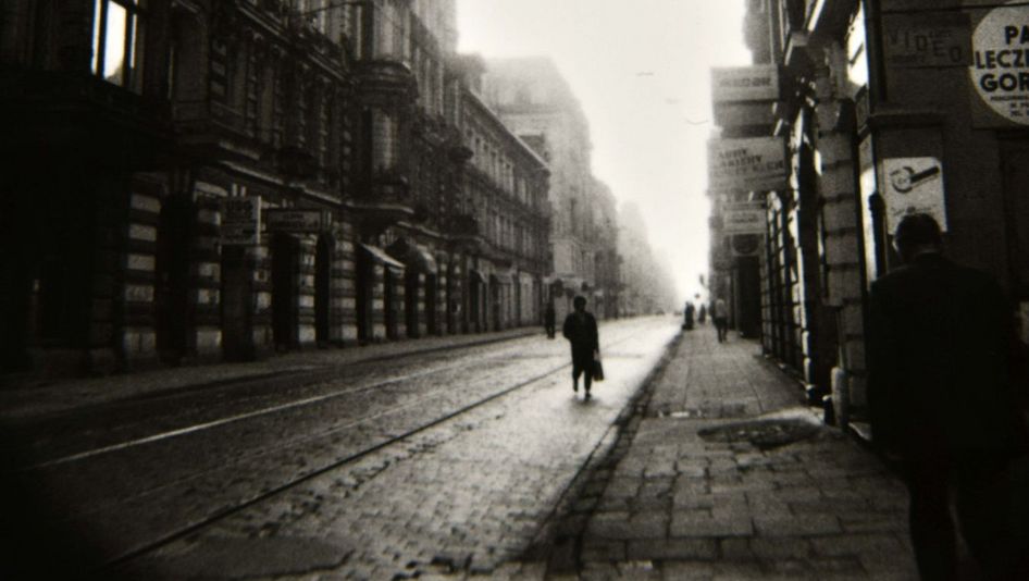 Filmstill aus LODZ SYMPHONY: Eine düstere, enge Straße, darauf einige Menschen.