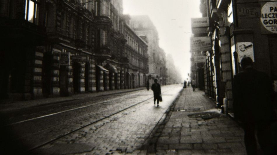 Film still from LODZ SYMPHONY: A gloomy, narrow street with a few people on it.