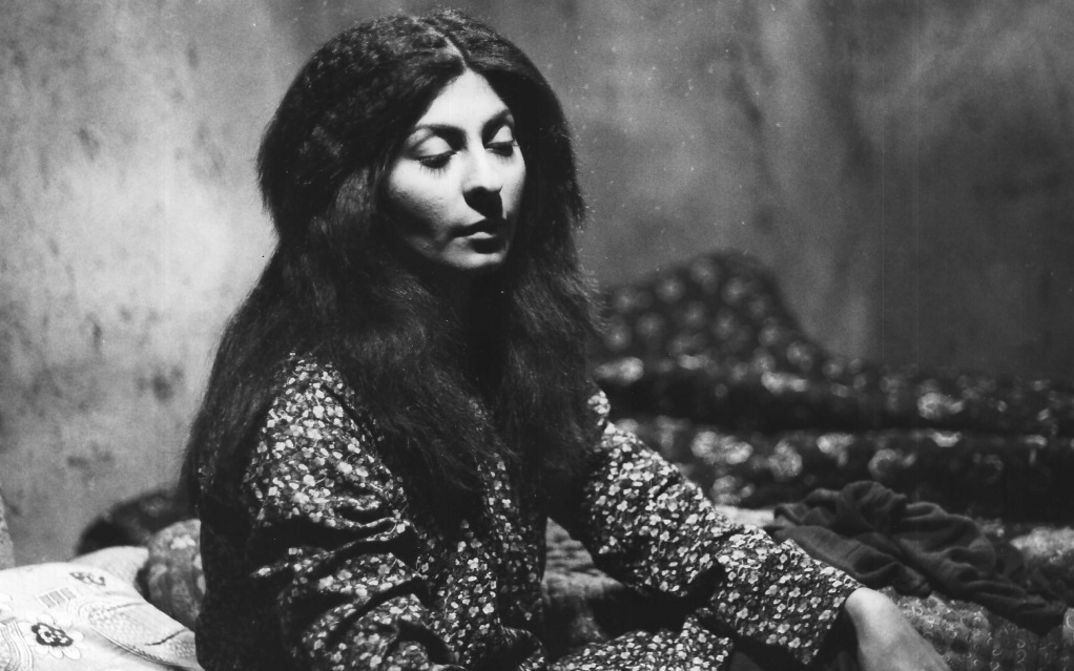 Film still from THE SEALED SOIL. A young woman with long hair sits in a room with half-closed eyes.