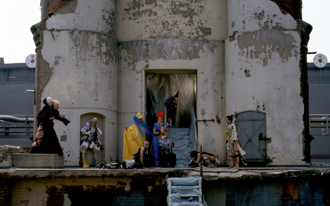 Film still from USINIMAGE: A group of people in imaginative costumes can be seen in front of a run-down industrial building.