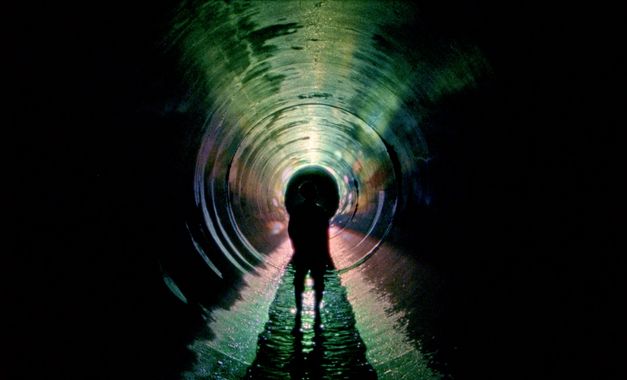 Film still from UNDERGROUND by Kaori Oda. The image shows the outline of a person in a long, dark tunnel. 