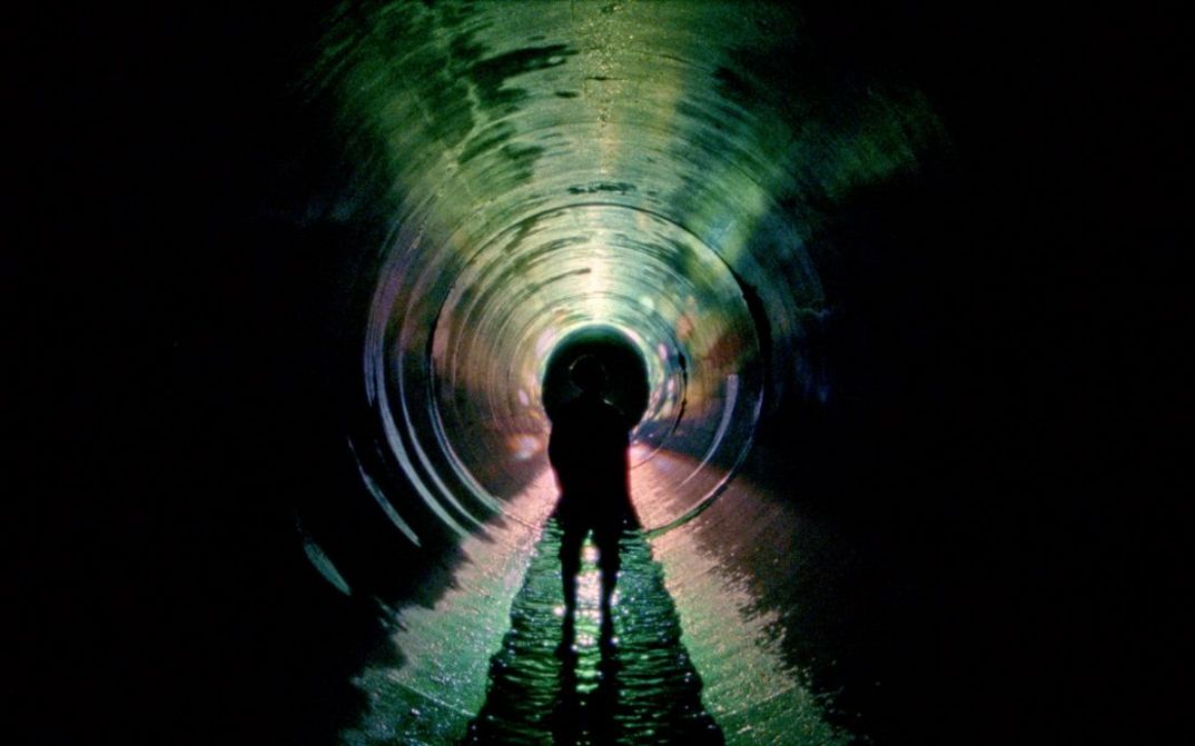 Film still from UNDERGROUND by Kaori Oda. The image shows the outline of a person in a long, dark tunnel.
