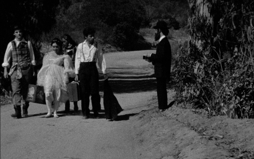 Film still from THE MAN WITHOUT A WORLD: A few people are walking down a street with their suitcases.