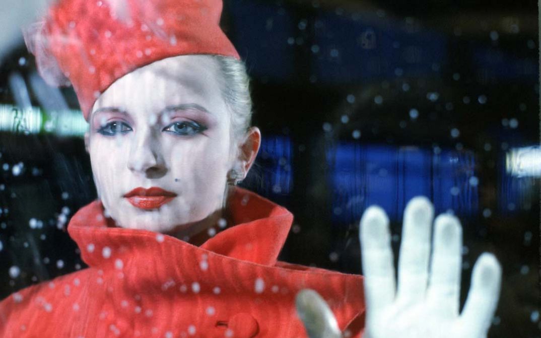 Film still from BILDNIS EINER TRINKERIN. An elegantly dressed woman looks through a pane of glass, you can see raindrops.