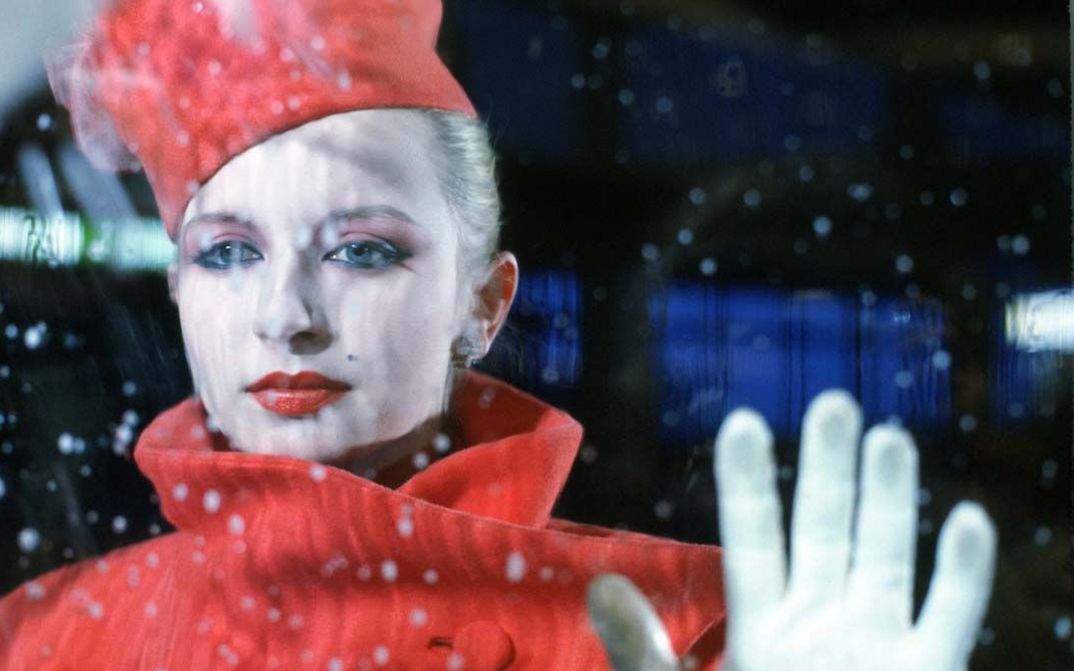 Film still from BILDNIS EINER TRINKERIN. An elegantly dressed woman looks through a pane of glass, you can see raindrops.