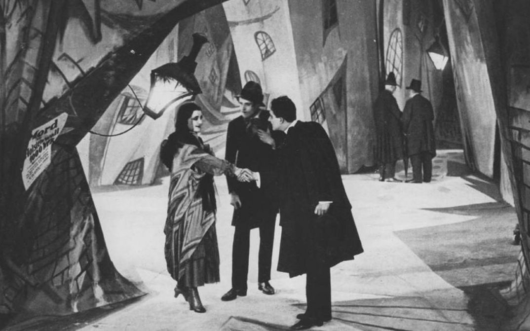 Film still from DAS CABINET DES DR. CALIGARI: A street scene with painted backdrops. A man and a woman shake hands.