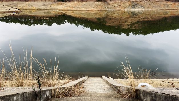 Film still from FRUIT FARM by Nana Xu. The image shows a stone staircase leading to a river in which a landscape is reflected. eigt eine Steintreppe, die zu einem Fluss führt, in dem sich eine Landschaft spiegelt. 