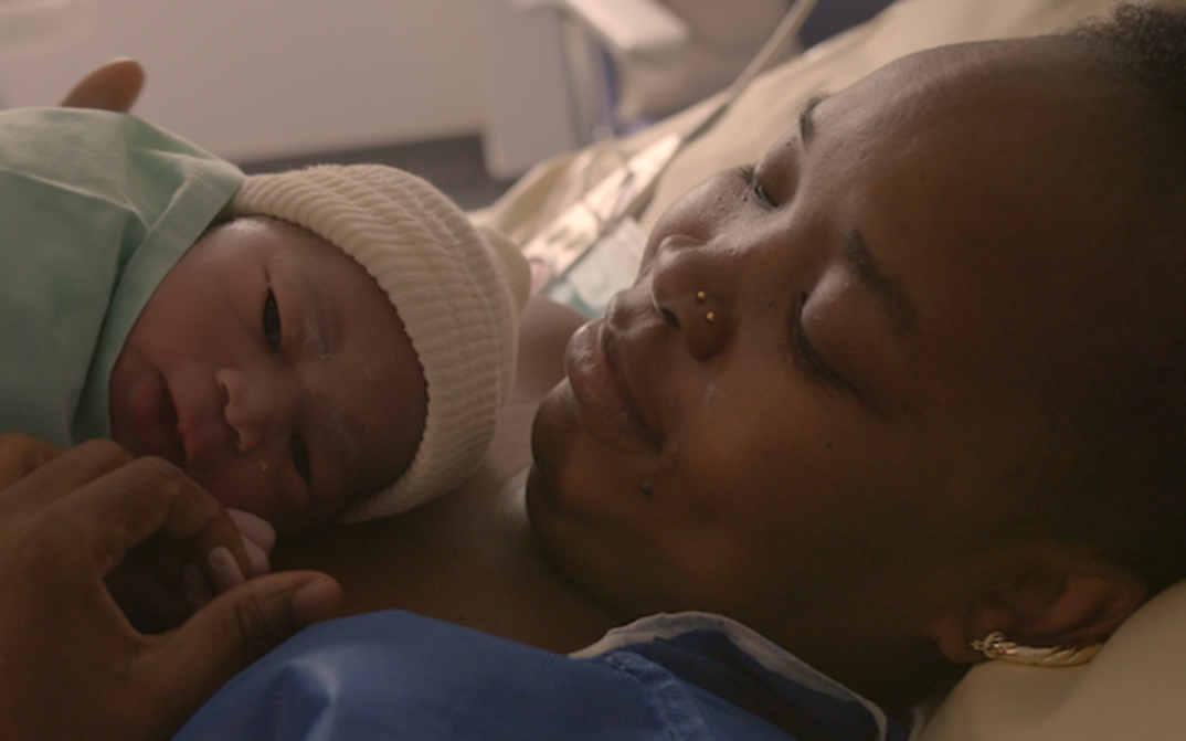 Film still from NOTRE CORPS: A mother with her newborn baby in a hospital bed.