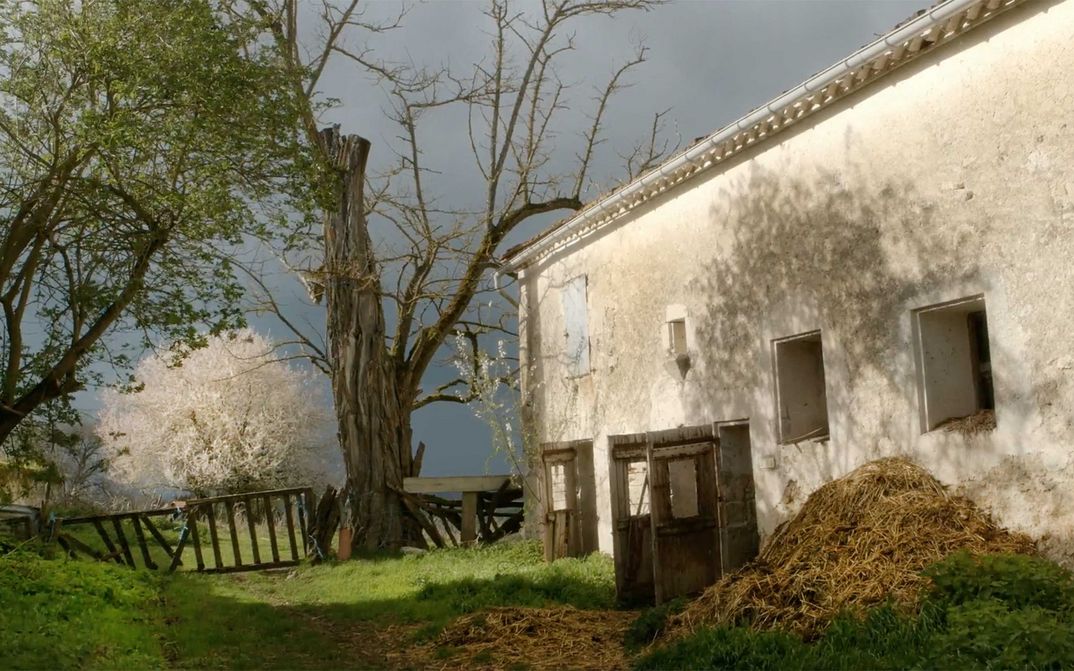 Film still from DIE FABELHAFTE WELT DES DR. CADÉOT: A whitewashed stable building with manure in front of it, you can also see trees and a fence.