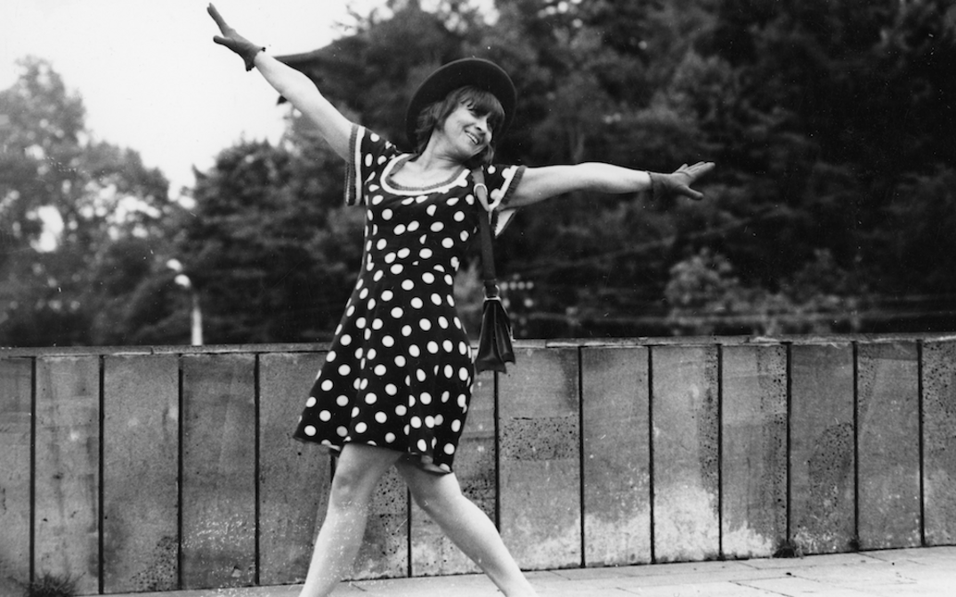Film still from COMMOTION: A woman in a polka-dot dress dances across the street.