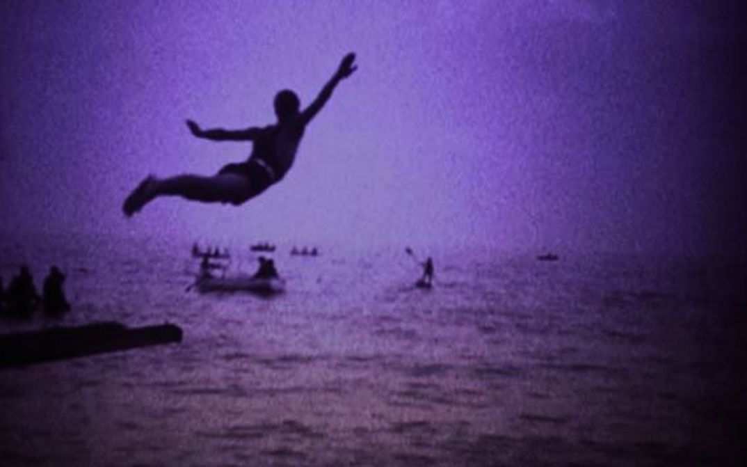 Film still from LA BOCCA DEL LUPO: Monochrome coloured image of a man jumping into the sea.