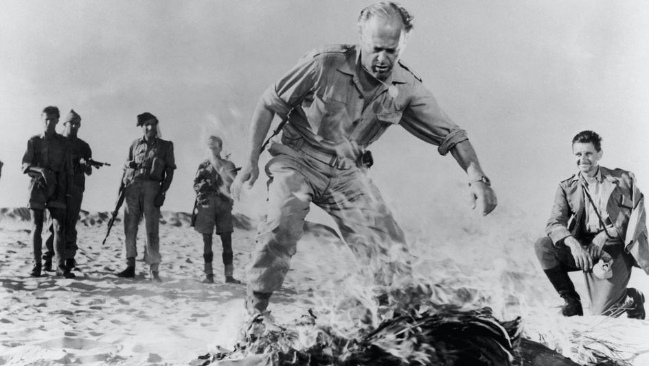 Film still from BITTER VICTORY: A few men in military uniforms in the desert stand around a fire.