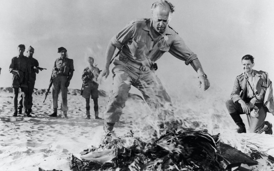 Filmstill aus BITTER VICTORY: Ein paar Männer in Militäruniformen in der Wüste stehen um ein Feuer herum.