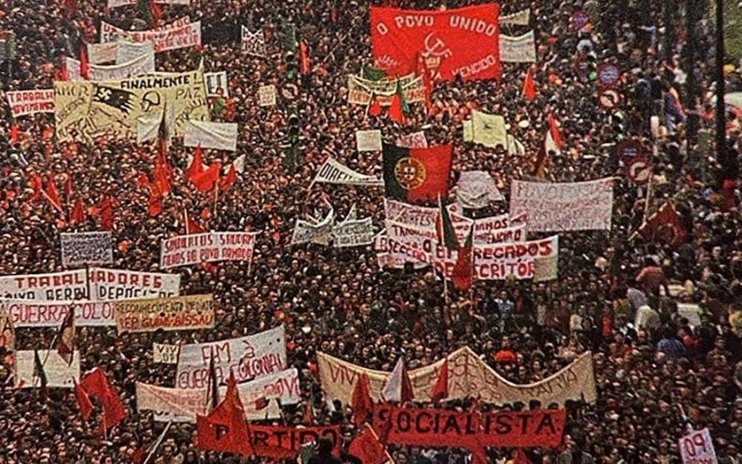 Film still from AS ARMAS E O POVO: You can see the crowd at a huge demonstration. Many have large banners or flags with them.