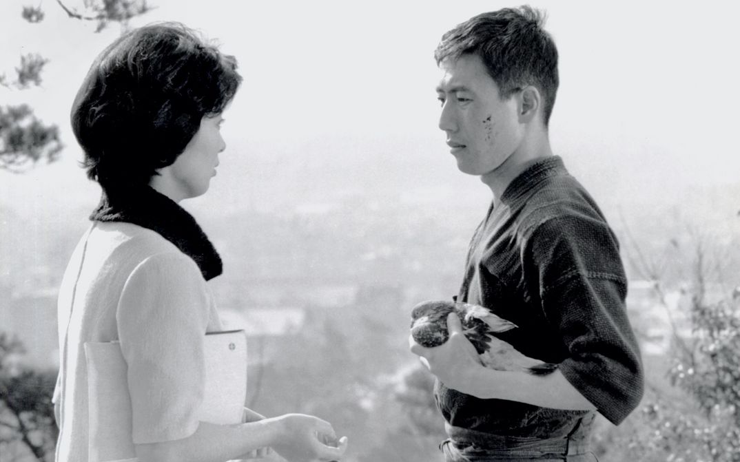 Film still from KEN: A man and a woman look at each other. He is wearing a kimono and holding an injured bird in his hands.