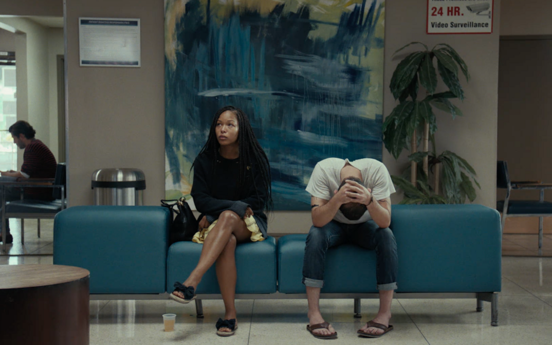 Film still from TEST PATTERN: A young couple sits side by side in a waiting room on a blue sofa.