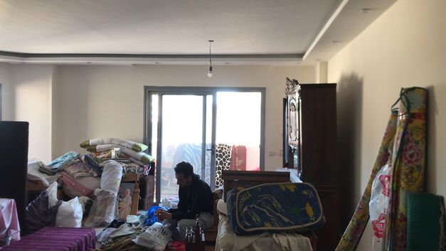 Film still from Mahmoud Ibrahim film’s “Akher Youm”. In a living room cluttered with boxes and furniture awaiting removal, a man sits amidst the impending chaos.