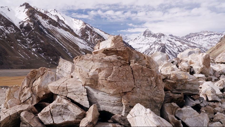 Filmstill aus THE CORDILLERA OF DREAMS: Ein rissiger Gesteinshaufen. Im Hintergrund teils schneebedeckte Berge.