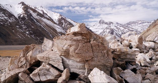 Filmstill from THE CORDILLERA OF DREAMS: A cracked pile of rocks. Partly snow-covered mountains in the background.