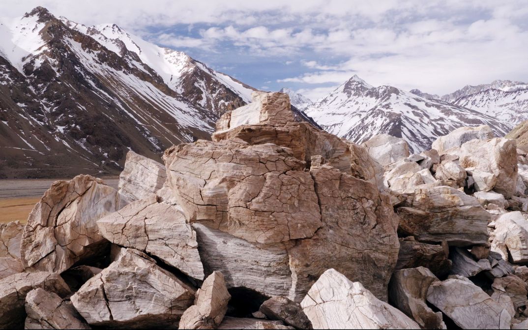 Filmstill from THE CORDILLERA OF DREAMS: A cracked pile of rocks. Partly snow-covered mountains in the background.