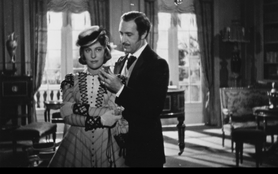 Film still from ROMANZE IN MOLL: A man and a woman, both elegantly dressed, in an upper-class apartment.