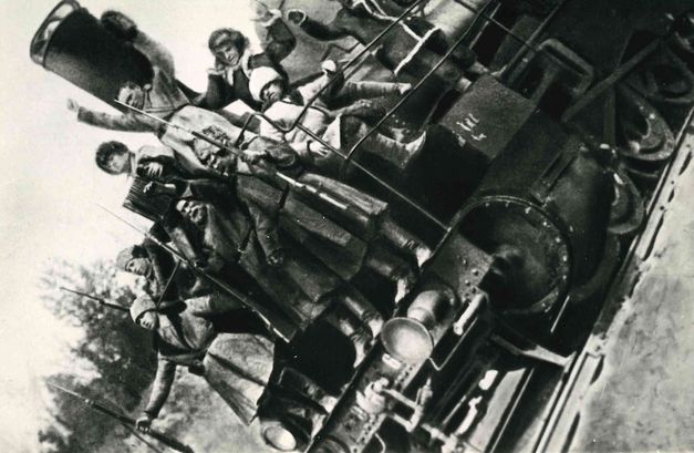 Film still from ARSENAL: Several men with rifles are standing on a locomotive. The picture is tilted to the left.