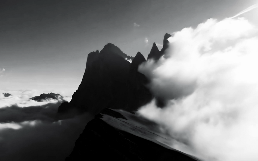 Film still from LA NATURE: The silhouettes of mountain peaks rise out of a cloud cover. On the left is a large cloud.