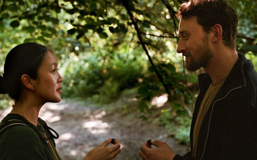 Film still from HERE: Two people look at each other, standing in a forest.