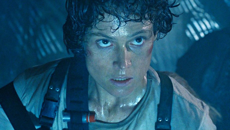 Film still from ALIENS: A woman, covered in sweat and armed with a cartridge belt, in a bluish-dark room.