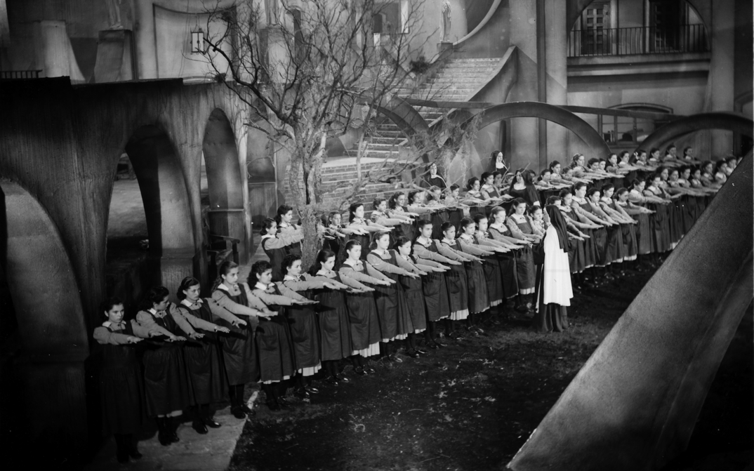 Film still from MUCHACHAS DE UNIFORME: Schoolgirls in uniform are lined up in an expressionist setting. A nun inspects their outstretched hands.