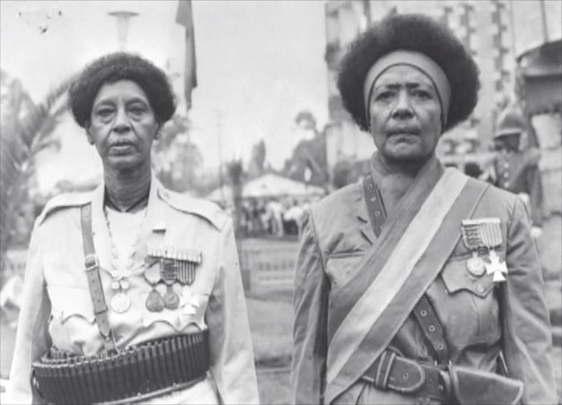 Historische Schwarzweißaufnahme von zwei Frauen in Uniform mit Orden, stehend vor einer Menschenmenge.